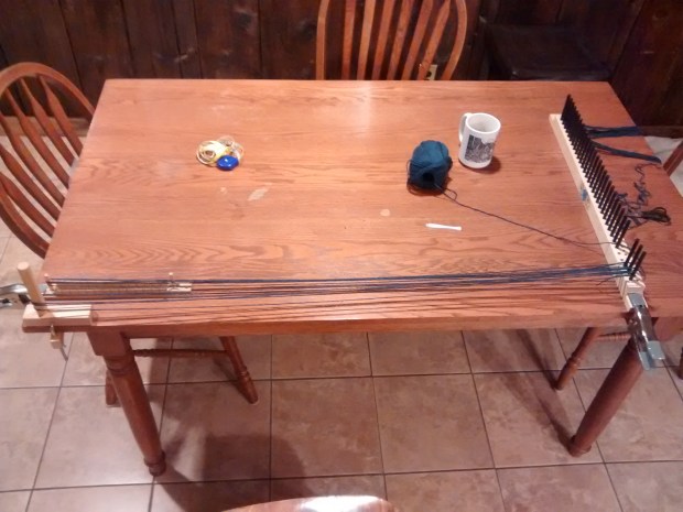 A picture of my warping process, using the peg loom itself, a warping peg, and a pompon rug loom on my kitchen table.